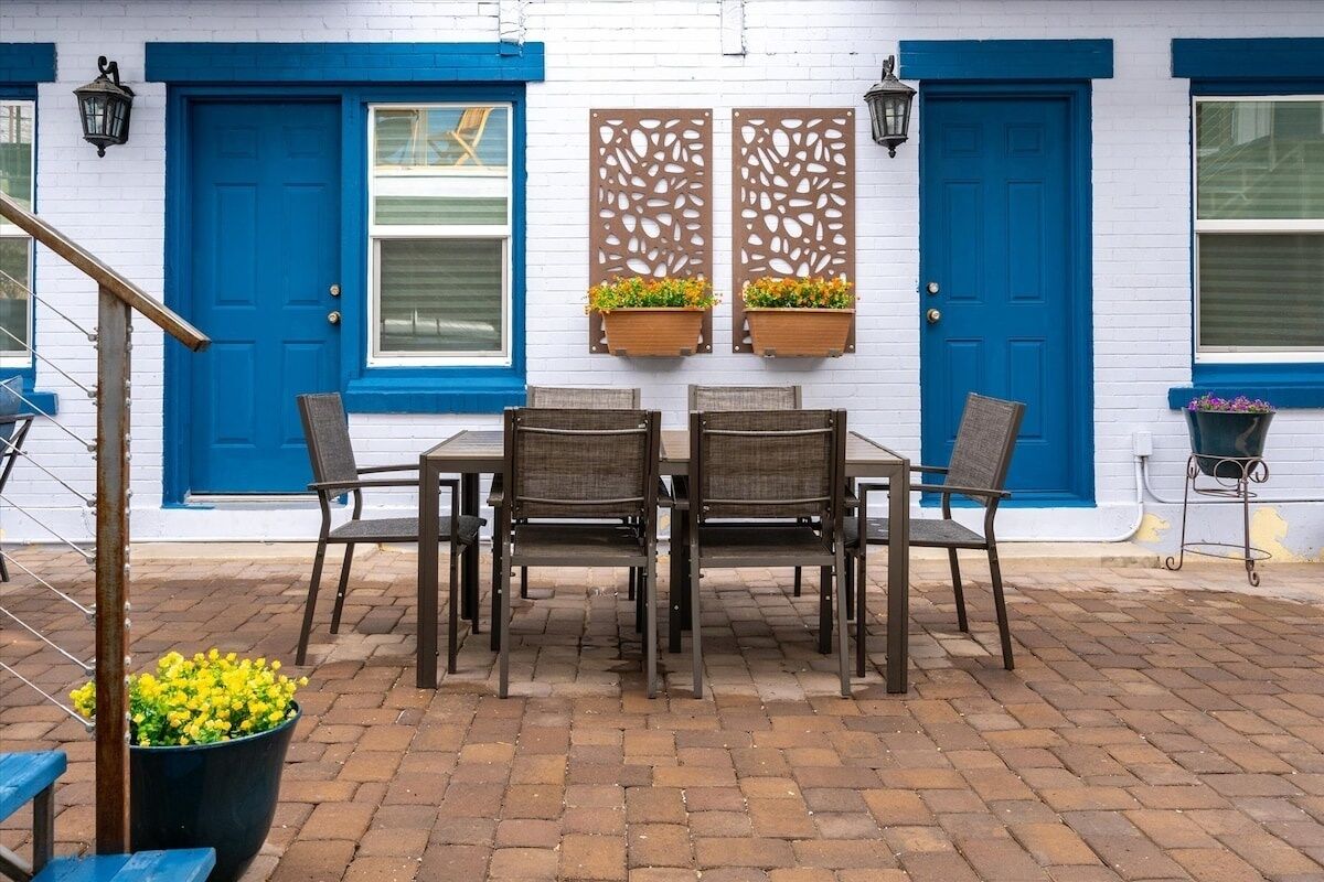 A patio with a table and chairs, a blue door, and a white wall with a window.