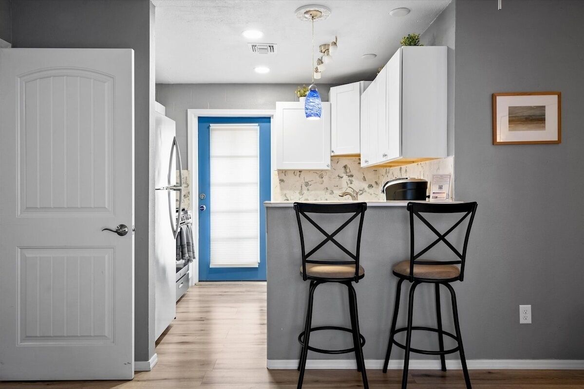 A kitchen with white cabinets, a marble countertop, two black bar stools, and a blue door in the background.