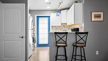A kitchen with white cabinets, a marble countertop, two black bar stools, and a blue door in the background.