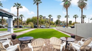 A patio area with white chairs and tables, a green lawn, and palm trees. - 11 Chelsea Place On The Park, In Heart Of Downtown (Phoenix)