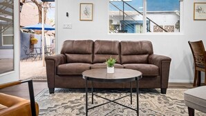 Ein braunes Ledersofa mit einem kleinen Tisch davor, einem gemusterten Teppich und einem Fenster mit Blick auf eine Treppe und einen Außenbereich.