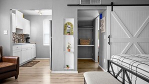Ein kompakter Wohnraum mit Küchenzeile, einem Bett mit Metallgestell, einem braunen Ledersessel und einer kleinen Bank.