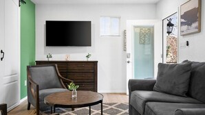 Uma sala de estar com televisão de tela plana, um sofá, uma poltrona, uma mesinha com uma planta e um armário.