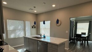 Une cuisine moderne dotée d’un îlot central, d’appareils électroménagers en acier inoxydable et de luminaires suspendus.
