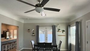 Un coin repas avec une table et des chaises, un ventilateur de plafond et une vue sur l’extérieur, accessible par une porte.