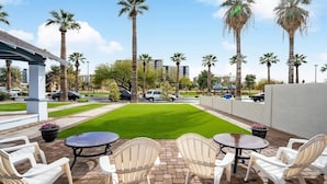 Un espace patio avec des chaises et des tables blanches, une pelouse verdoyante et des palmiers.