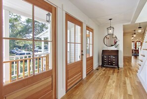 A hallway with wooden floors, large windows, and a wooden bench.