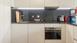 A modern kitchen with white cabinets, a black countertop, a toaster, a kettle, and a small oven. - Liiiving in Matosinhos - Warm Vintage Apartment (Matosinhos)