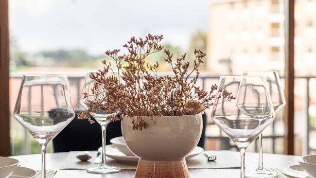 A dining table set with plates, cutlery, and wine glasses, with a vase of dried flowers in the center. - Liiiving in Matosinhos - Warm Vintage Apartment (Matosinhos)