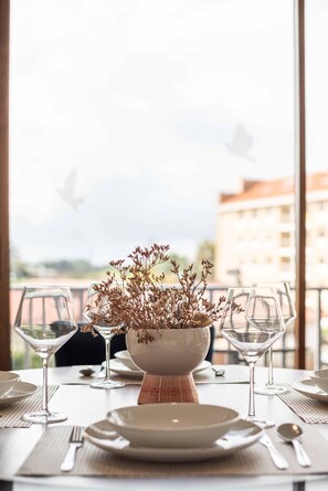 Una mesa de comedor dispuesta con platos, cubiertos y copas de vino, con un jarrón de flores secas en el centro.