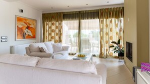 A modern living room with a sofa, a coffee table with fruit, a painting on the wall, and a TV. - La Casa Rosa Seaside Getaway (Dorida)