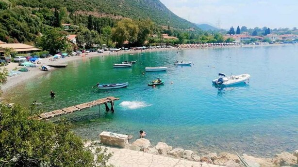 A clear lake with boats, a wooden dock, and a beach with umbrellas. - La Casa Rosa Seaside Getaway (Dorida)