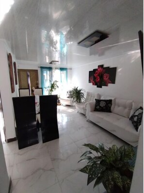 Uma sala de estar ampla com um sofá branco, uma mesa de centro e várias plantas em vasos.