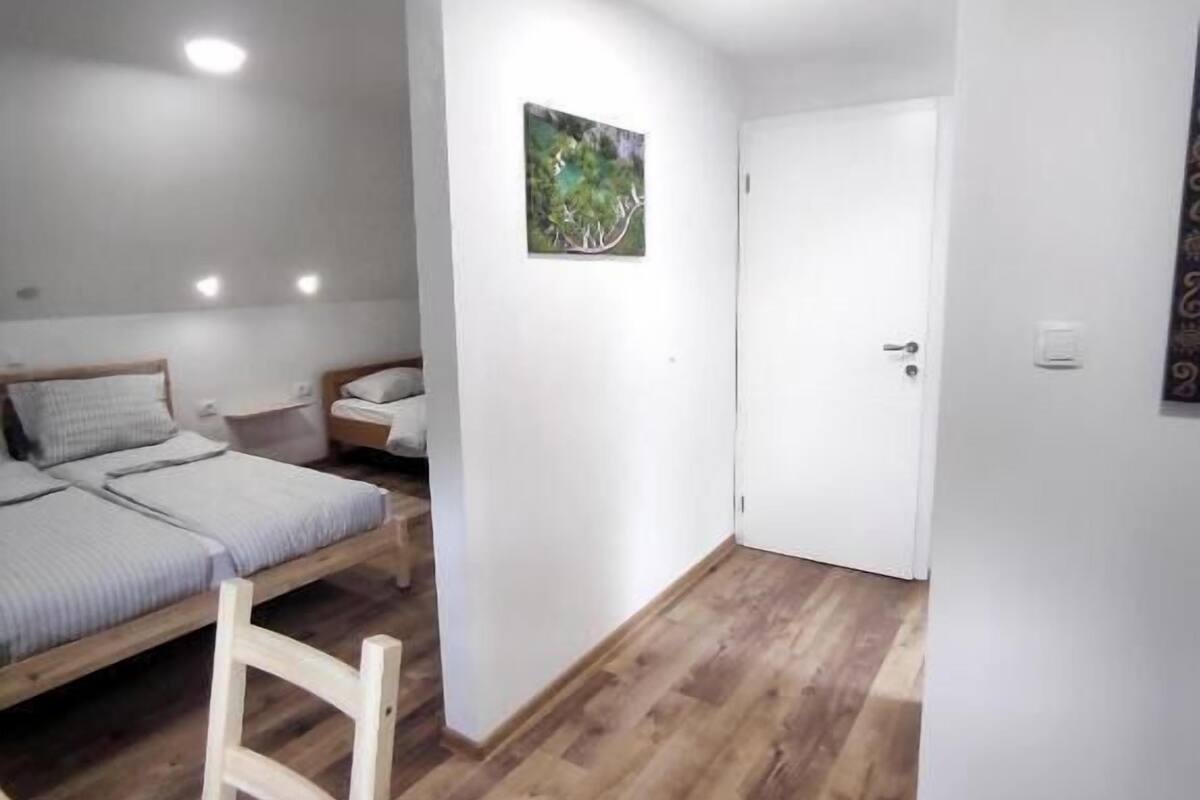 A bedroom with a bed, bedside tables, a chair, a door, and a small painting on the wall.