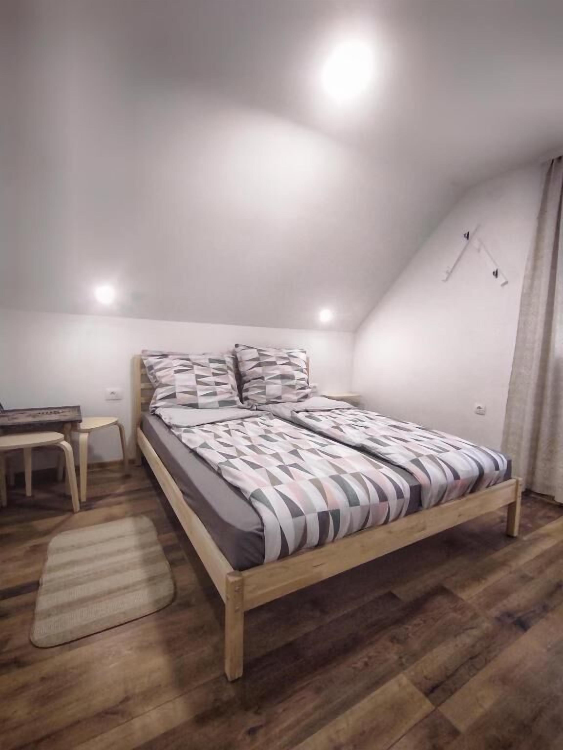 A bedroom with a wooden bed, a bedside table, a small desk, and a rug.
