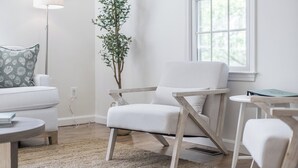 Un soggiorno moderno con un divano bianco, una poltrona in legno, un tavolino rotondo e una pianta in vaso.