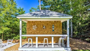 Un gazebo in legno con tetto bianco, un cartello di benvenuto e tre sgabelli bianchi.
