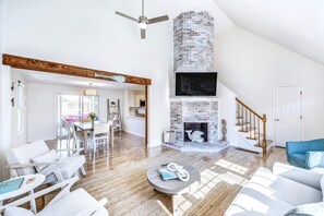 A spacious living area with a high ceiling, a fireplace, a dining area, and a staircase. - Luxury Getaway with Hot Tub!, Harwich Getaway with Hot Tub (Harwich)