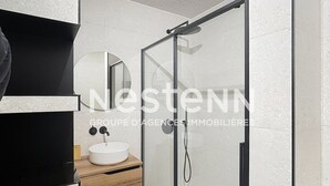 A modern bathroom with a glass shower enclosure, a white sink, and a wooden vanity. - Air-conditioned apartment with pool in Argelès-sur-Mer (Argelès-sur-Mer)
