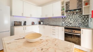 Eine moderne Küche mit weißen Schränken, einer Marmorarbeitsplatte, einem eingebauten Backofen und einer strukturierten Spritzschutzwand.