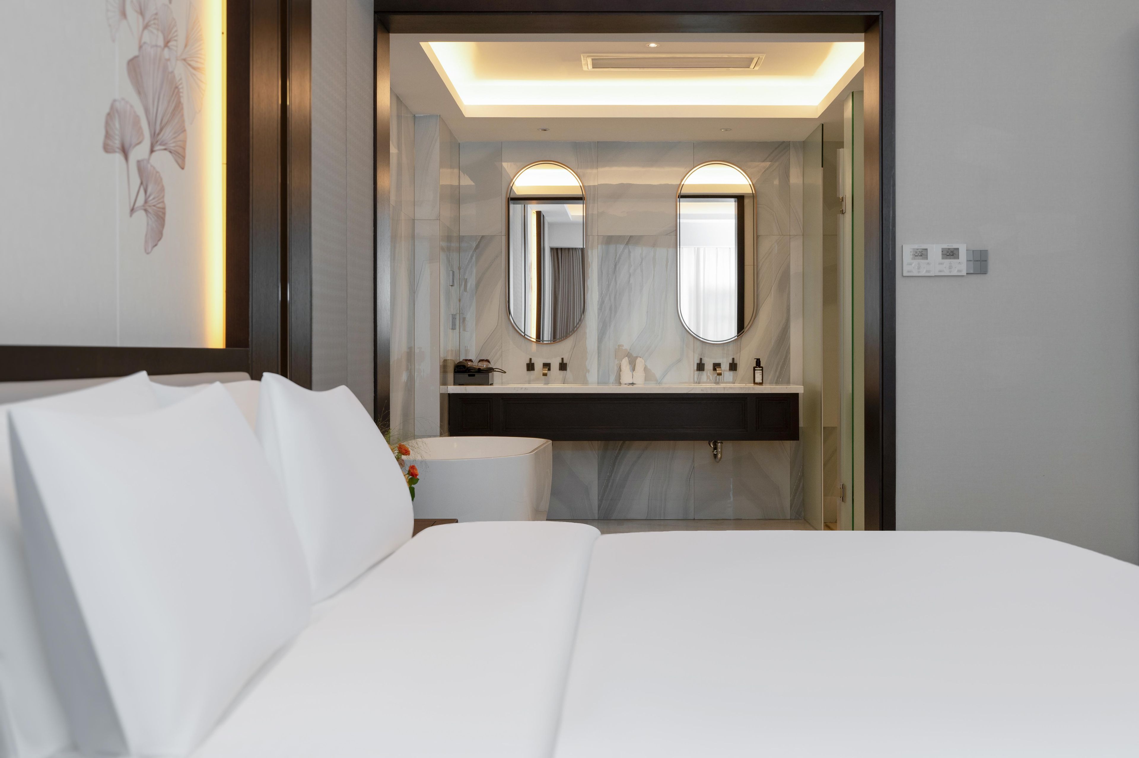 A modern hotel room with a large bed, a bathroom with two mirrors, a sink, and a toilet.