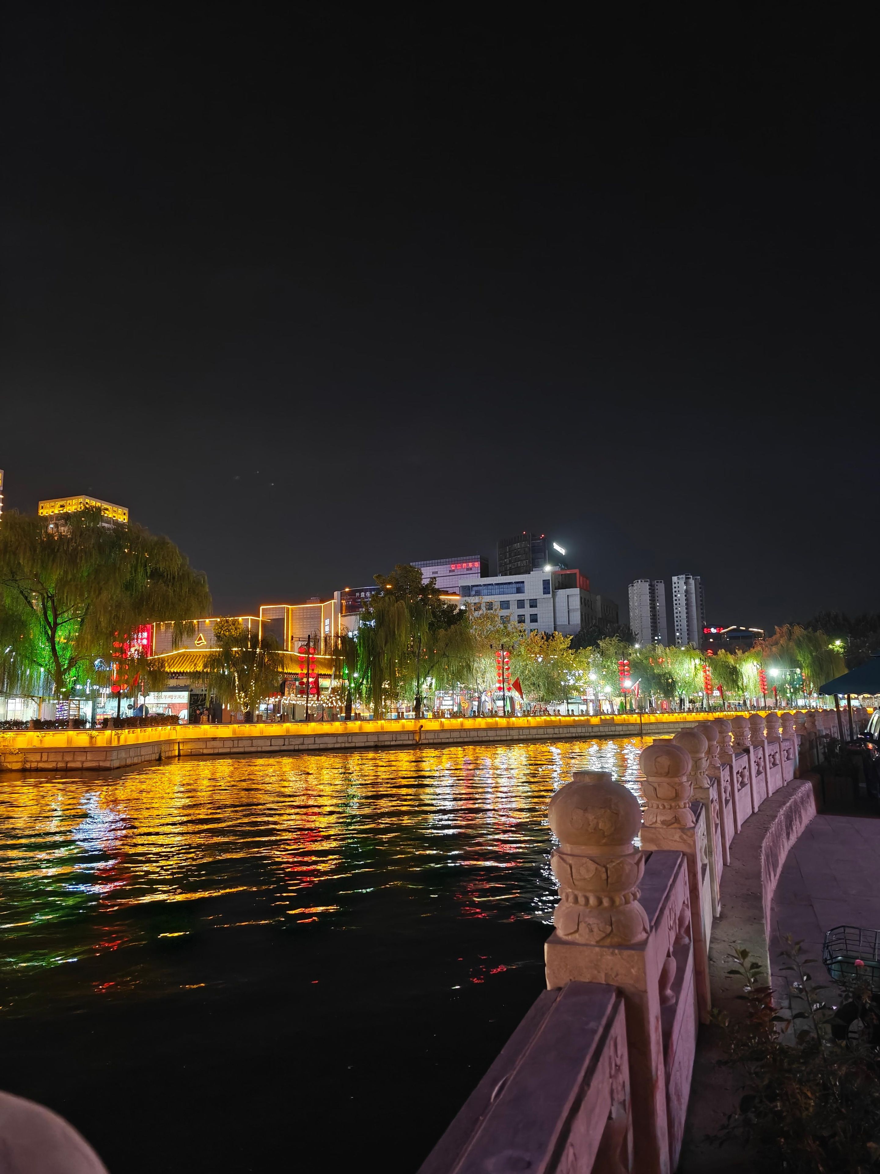 Ein nächtlicher Blick auf eine Uferpromenade mit beleuchteten Gebäuden und einer Steinbrüstung.