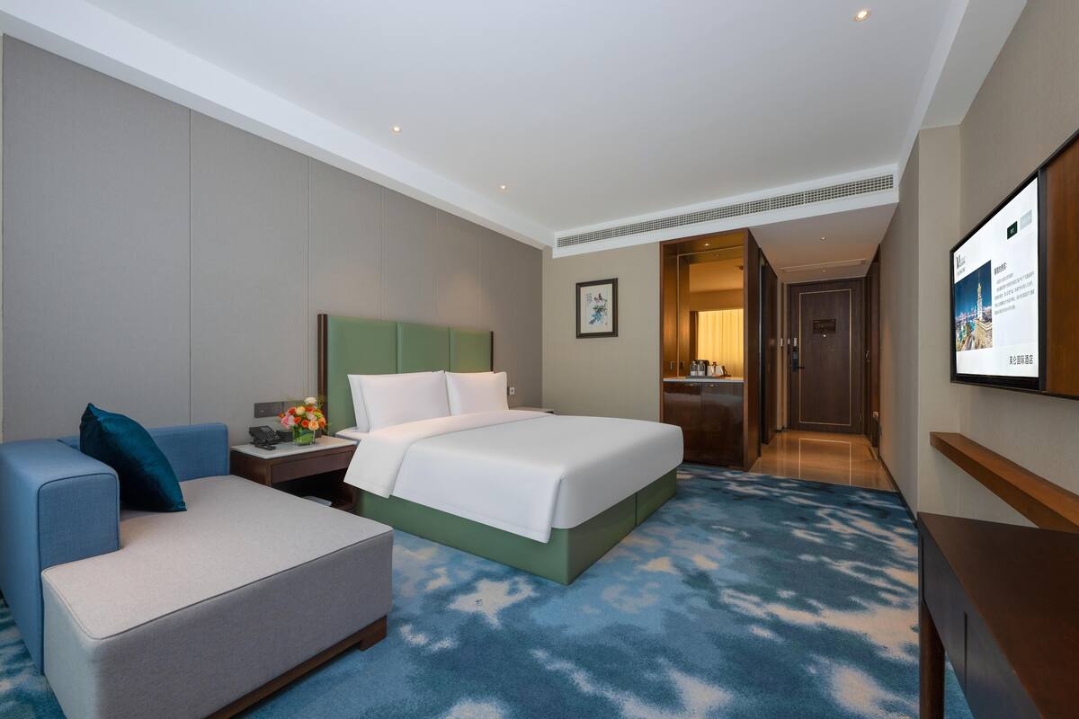 A hotel room with a bed, a desk, a chair, a TV, and a door leading to a bathroom.
