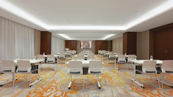 A conference room with rows of white tables and chairs, a patterned carpet, and a neutral color scheme.