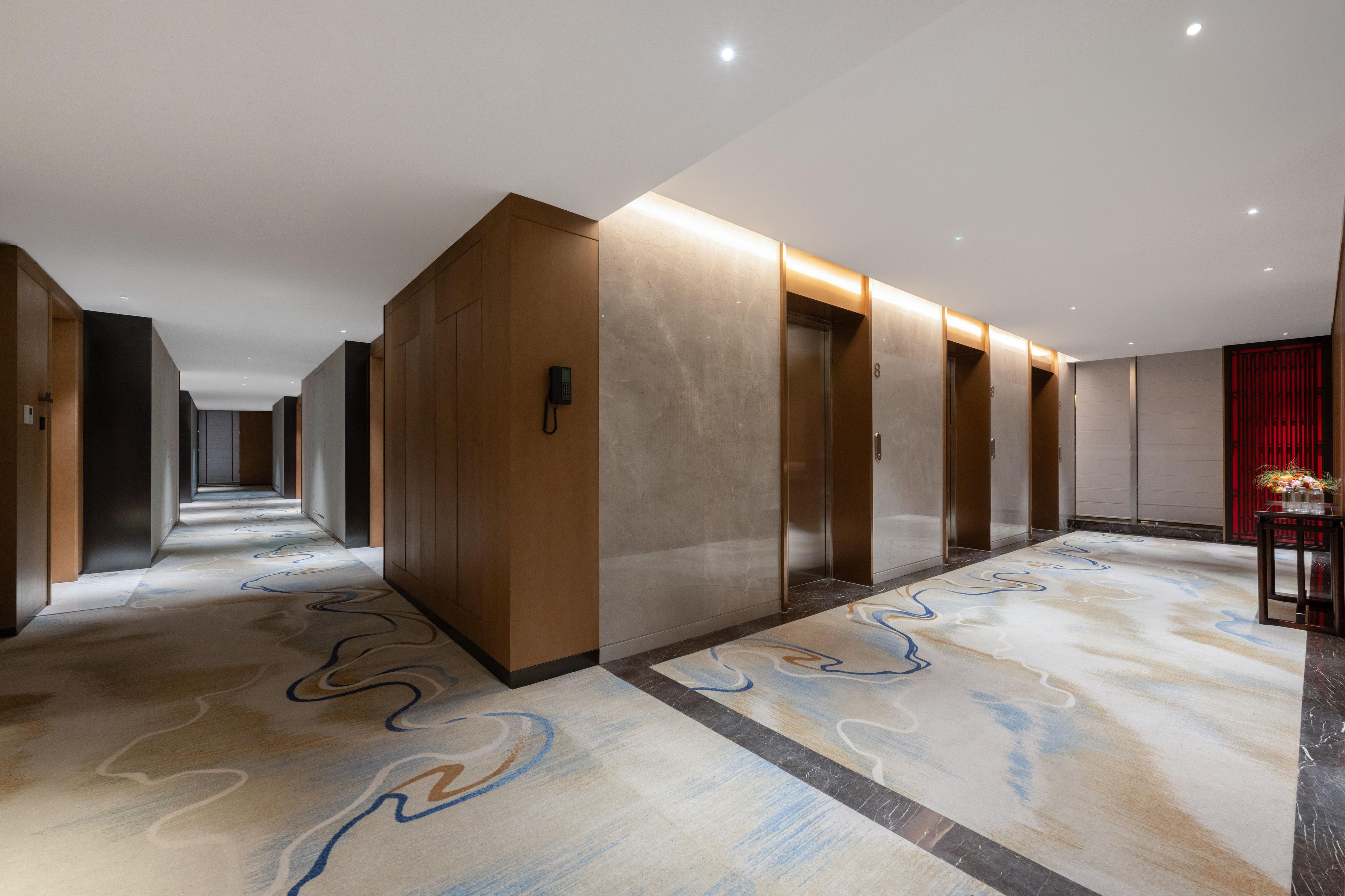 Un pasillo largo en un hotel, con puertas de madera y una alfombra estampada.
