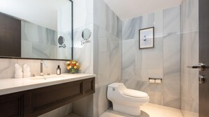 A modern bathroom with a marble wall, a white toilet, a large mirror, and a vanity with a sink and towel rack.