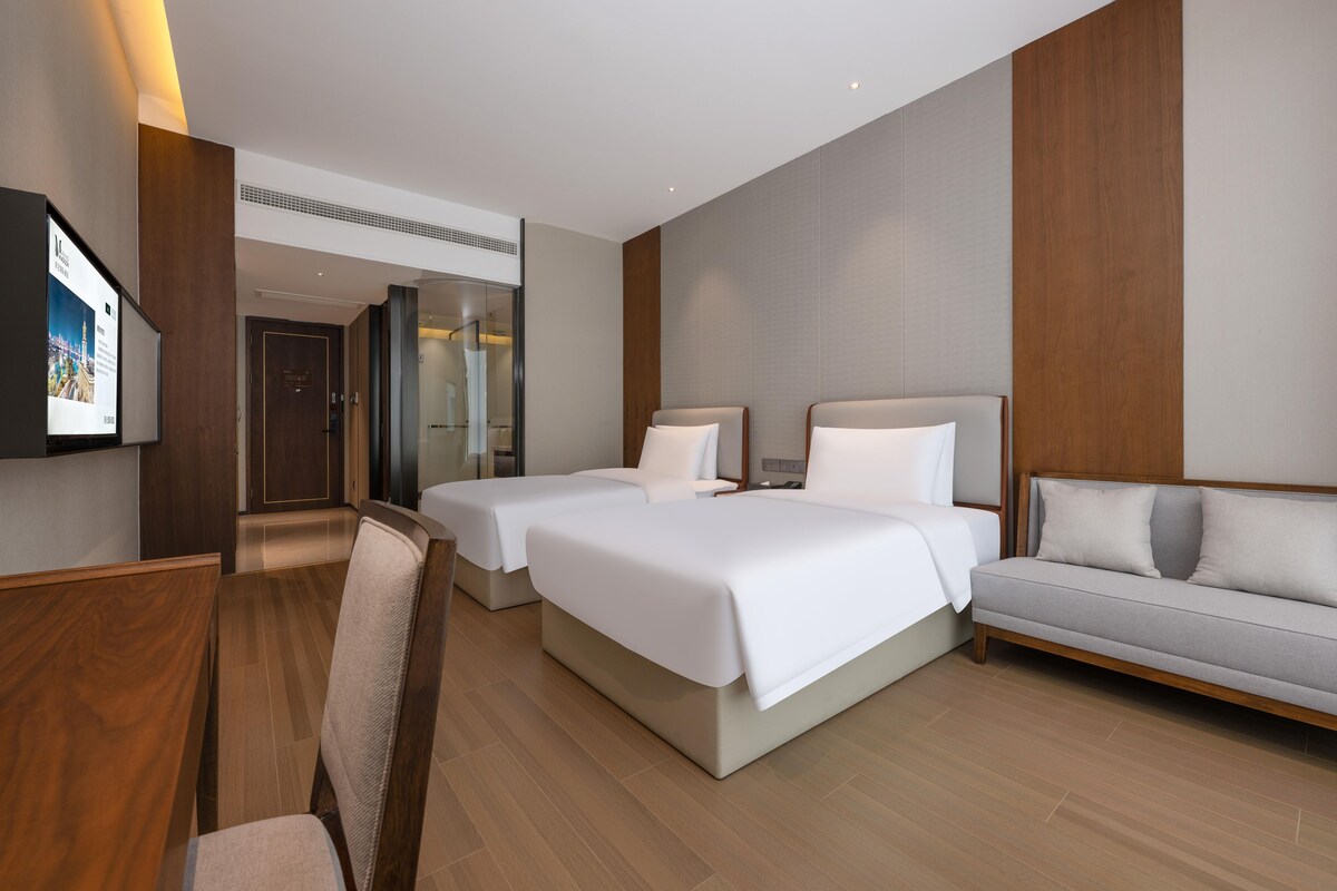 A hotel room with two beds, a sofa, a desk, and a TV.