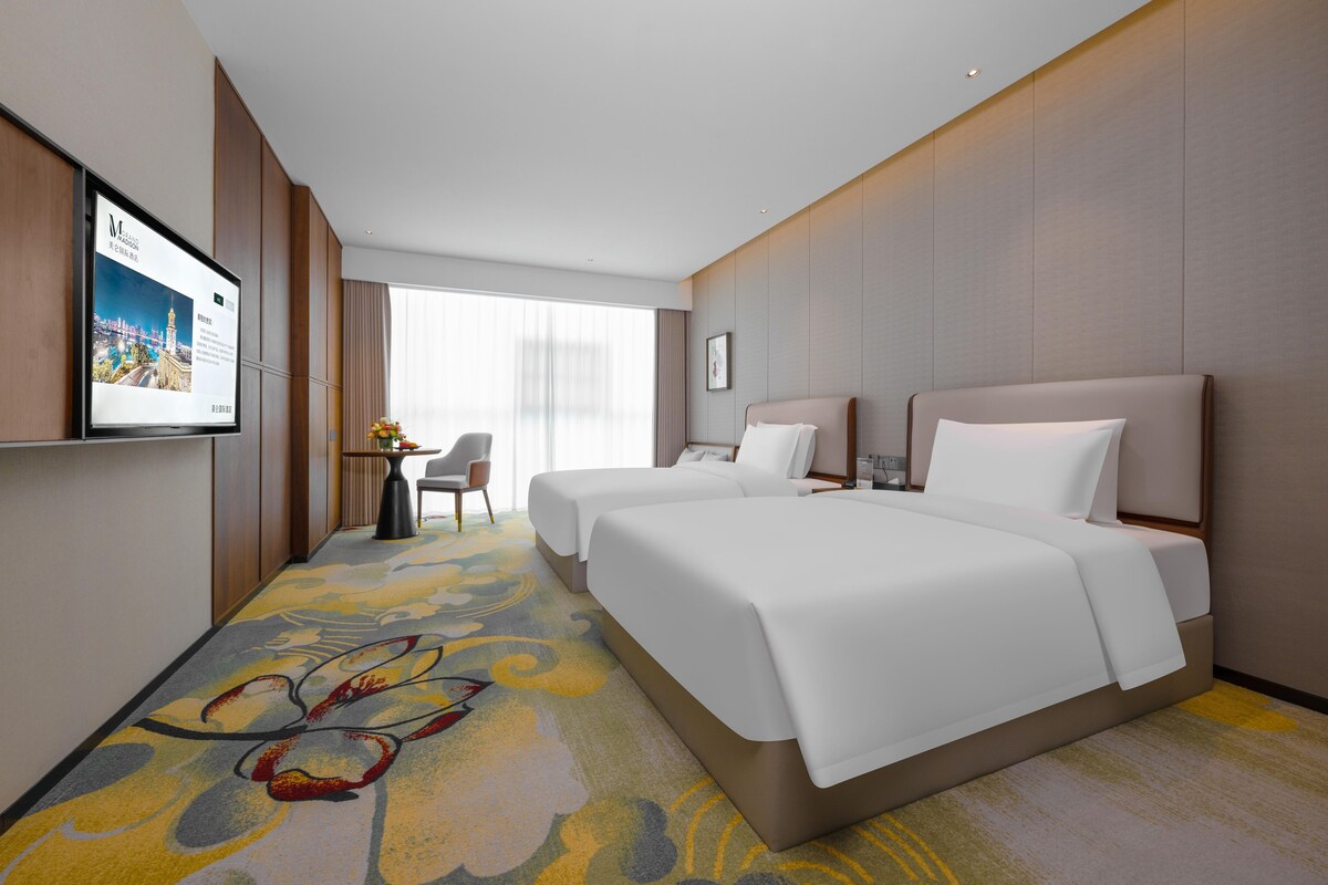 A hotel room with a large bed, a desk, a chair, and a television on the wall.