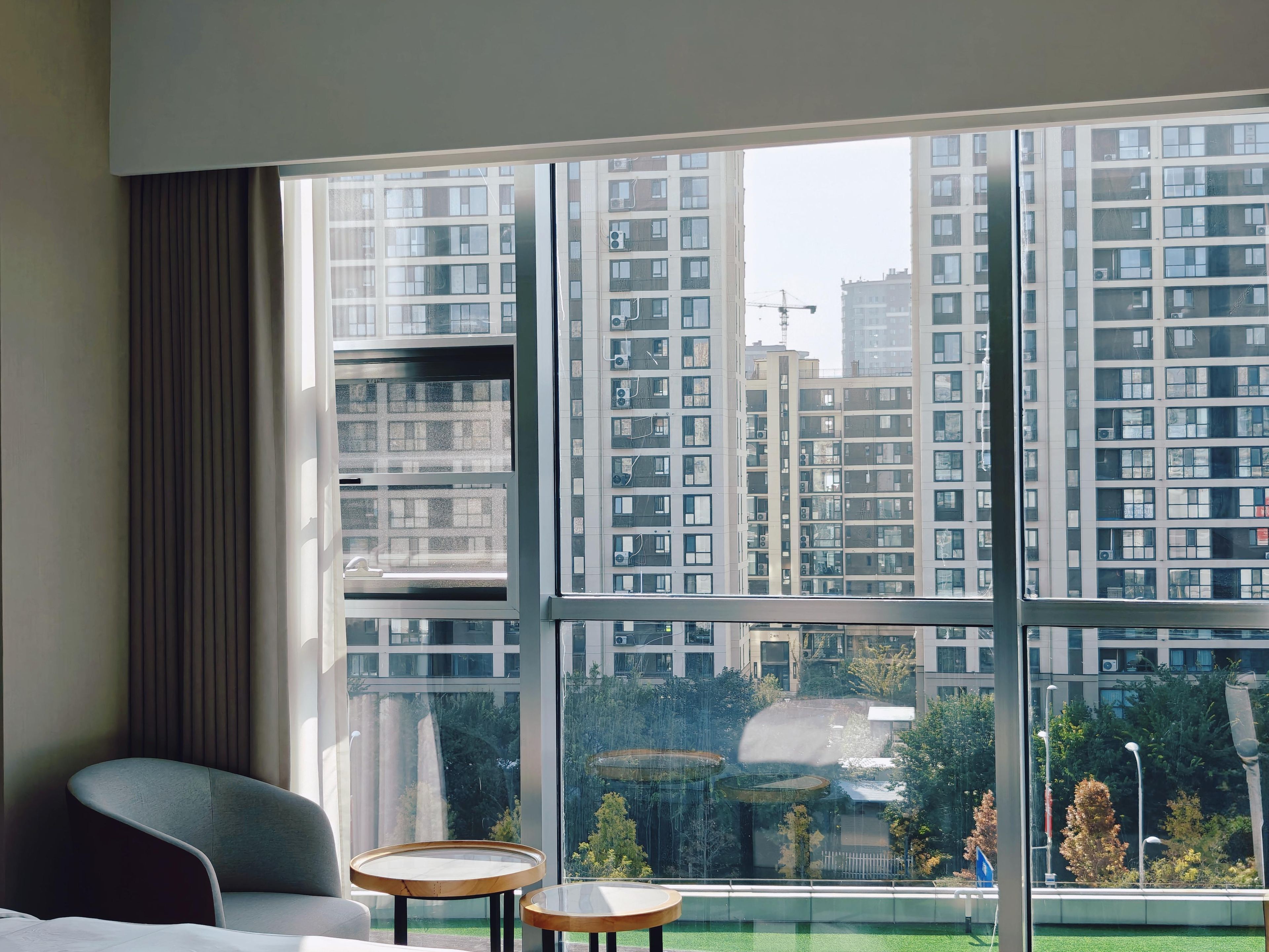 Ein Hotelzimmer mit großem Fenster, einem grauen Sessel, einem kleinen runden Tisch und einem Bett.