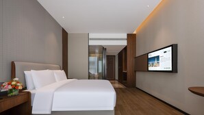 A hotel room with a large bed, a flat-screen TV mounted on the wall, and a wooden floor.