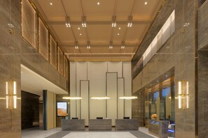 Een moderne lobby met marmeren vloeren, een receptiebalie en een digitaal scherm.