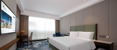 Une chambre d’hôtel avec un grand lit, un bureau avec une chaise, un téléviseur fixé au mur et une fenêtre avec des rideaux.