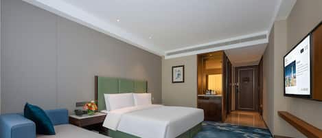A hotel room with a bed, a desk, a chair, a TV, and a door leading to a bathroom.