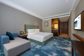 Een hotelkamer met een bed, een bureau, een stoel, een televisie en een deur naar een badkamer.