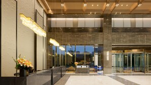 A modern hotel lobby with a reception desk, a glass revolving door, and a large window offering a view of the cityscape.