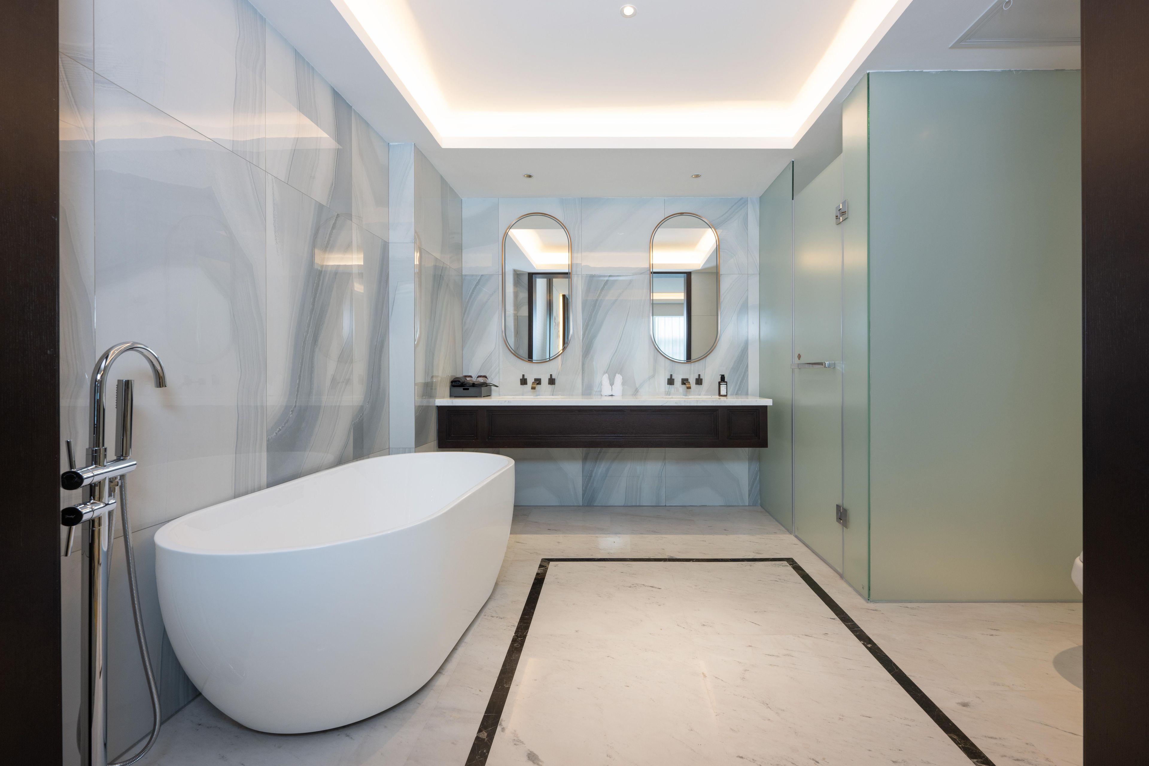 Un baño moderno con una bañera independiente, una ducha con cerramiento de vidrio y un lavamanos con dos espejos.
