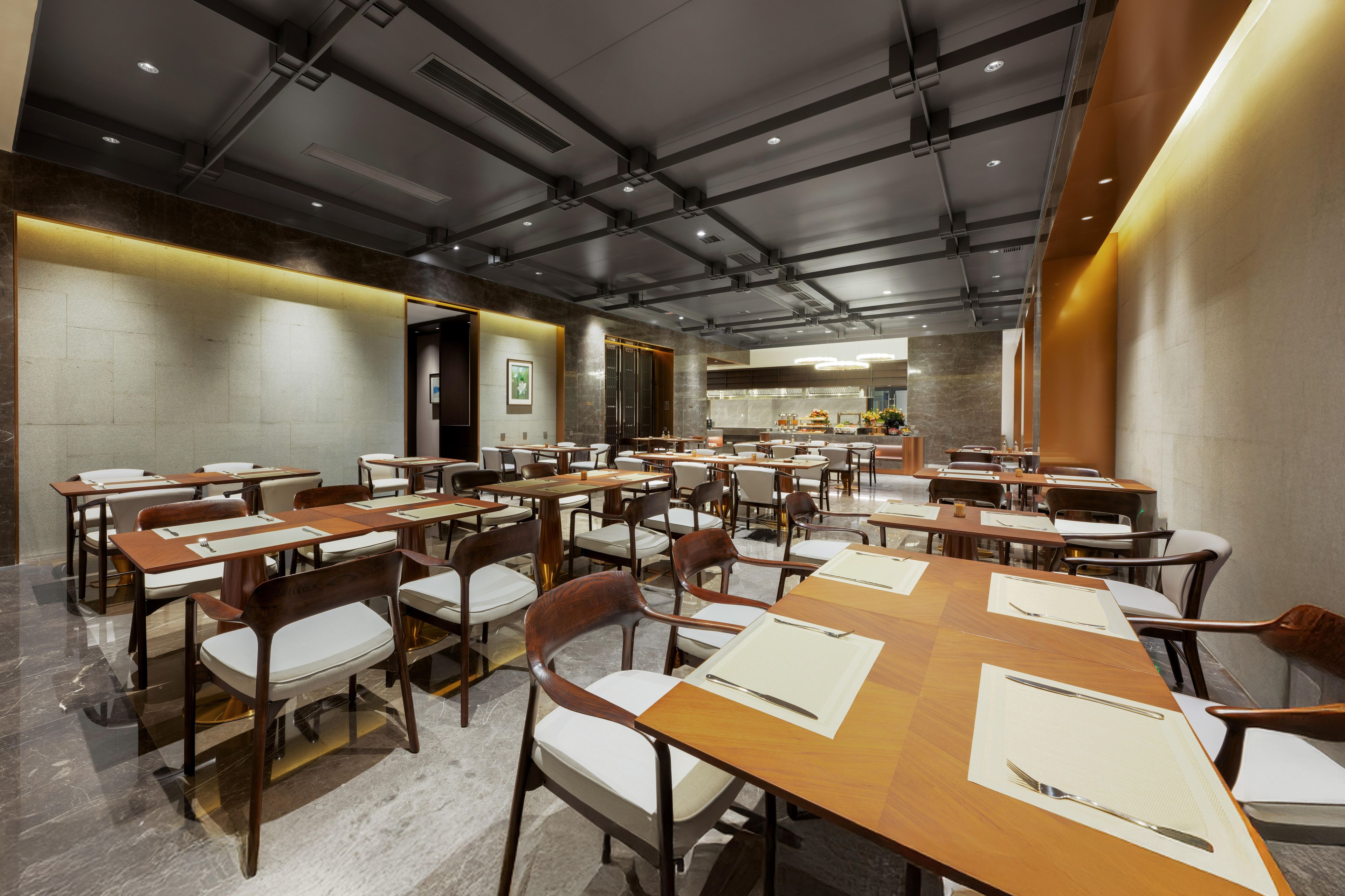 A spacious dining area with multiple tables and chairs, a kitchen in the background, and a modern ceiling design.
