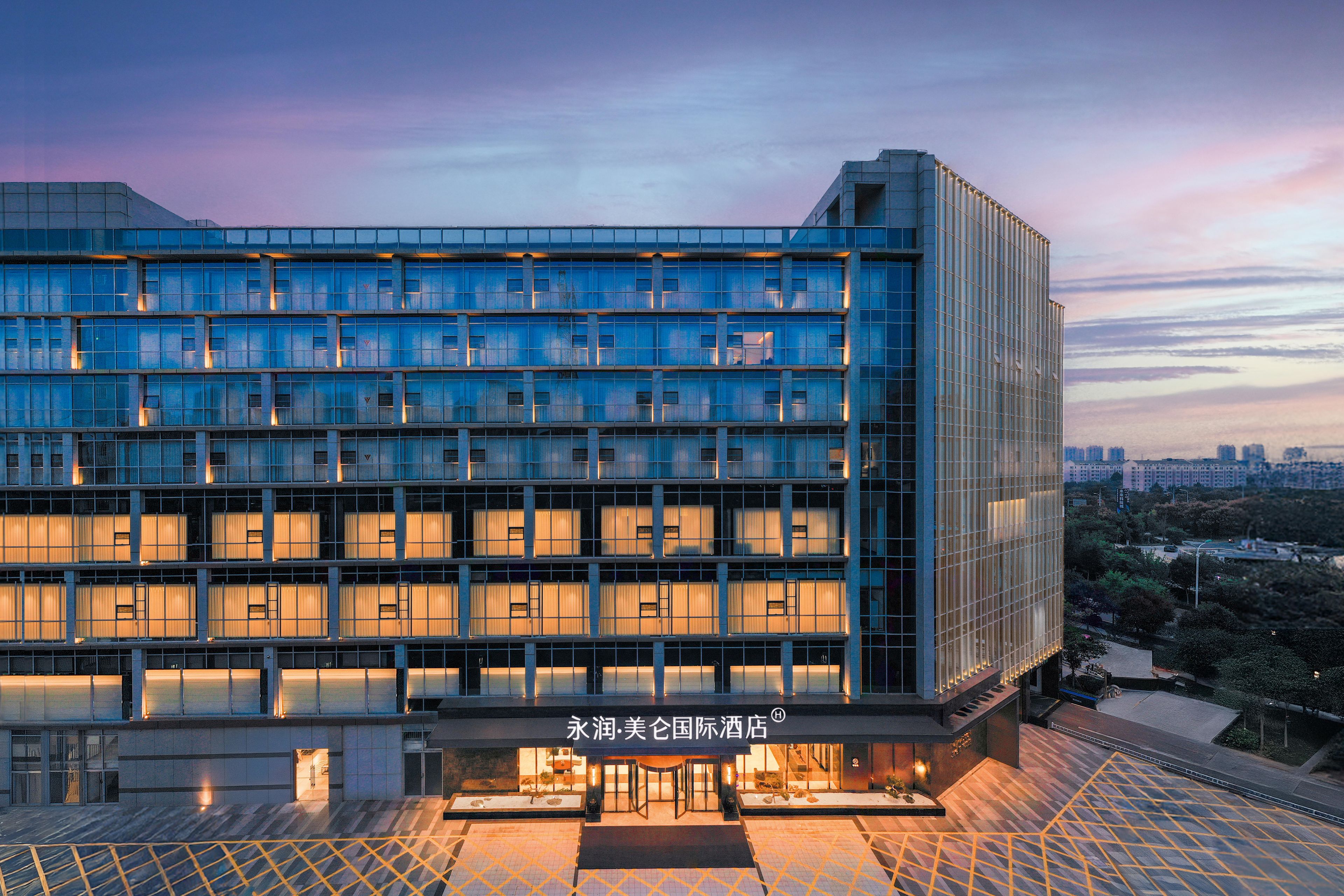 A modern hotel with a glass facade, multiple floors, and a well-lit entrance.