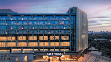 A modern hotel with a glass facade, multiple floors, and a well-lit entrance.