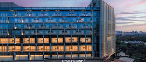 A modern hotel with a glass facade, multiple floors, and a well-lit entrance.