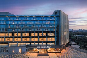 Een modern hotel met een glazen gevel, meerdere verdiepingen en een goed verlichte ingang.