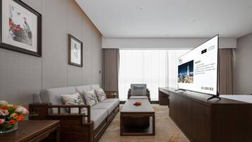 A modern hotel room with a sofa, a coffee table, a TV, and a desk with a monitor.