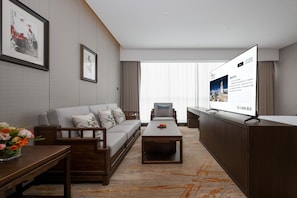 Una habitación de hotel moderna con sofá, una mesa de centro, televisor y escritorio con monitor.