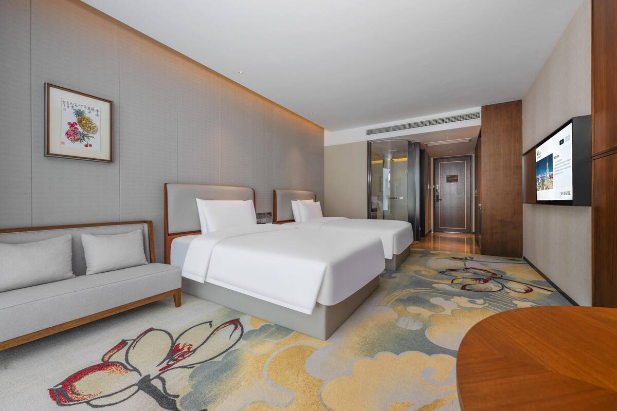 A hotel room with a bed, a sofa, a TV, and a carpet with a floral pattern.