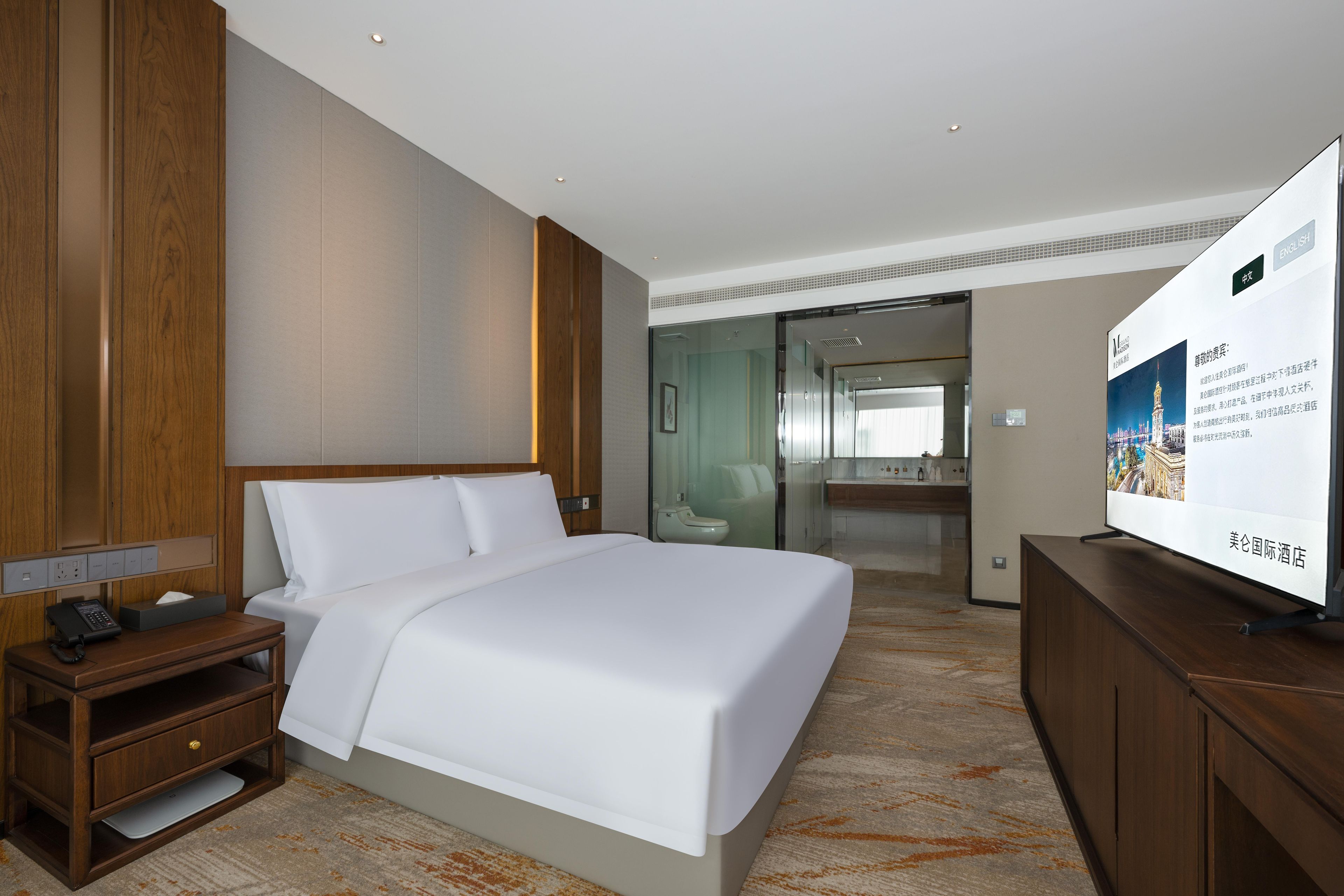 A hotel room with a large bed, wooden nightstand, and a television on a wooden cabinet.