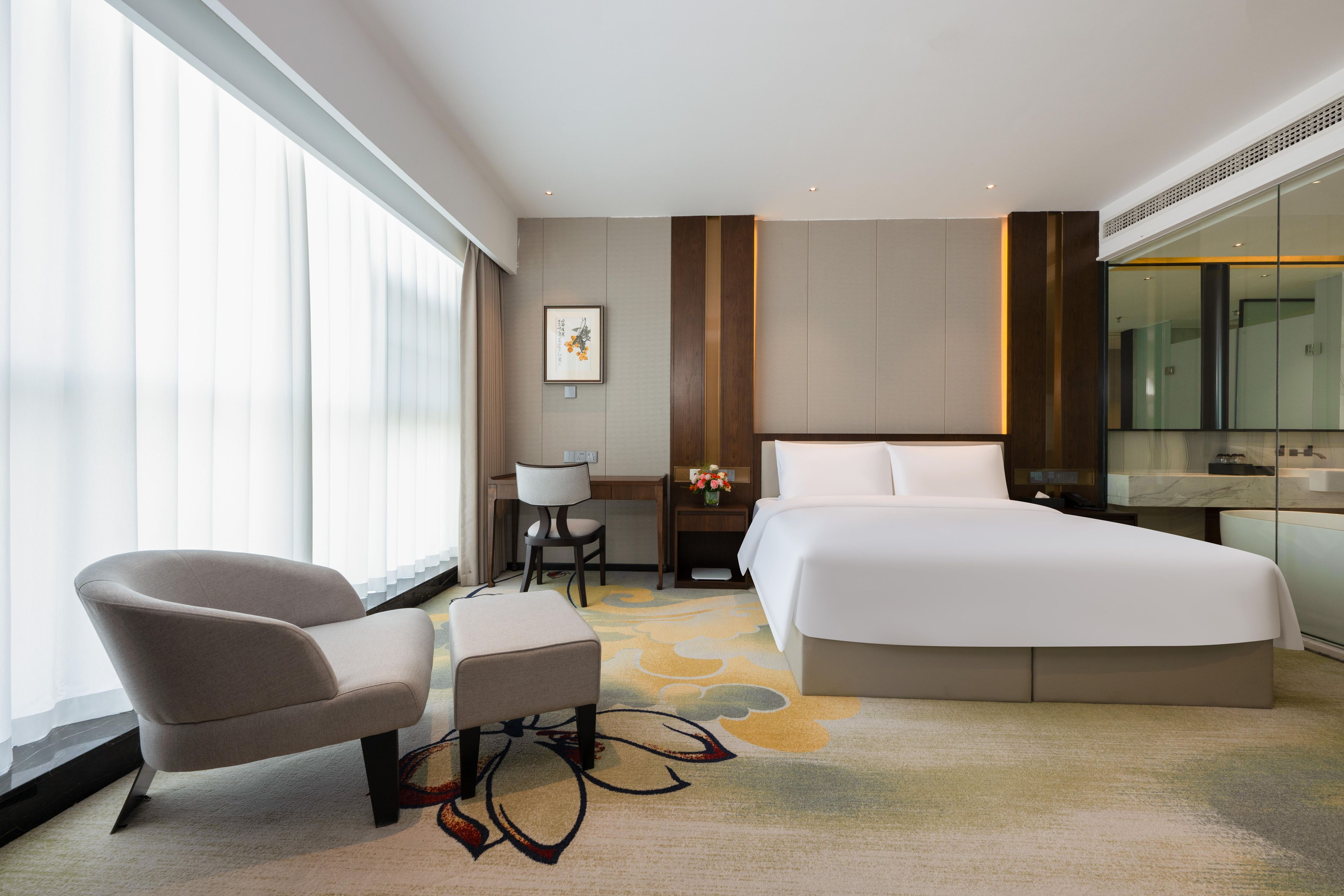 Habitación de hotel moderna con una cama grande, un escritorio, una silla y un ventanal con persianas.